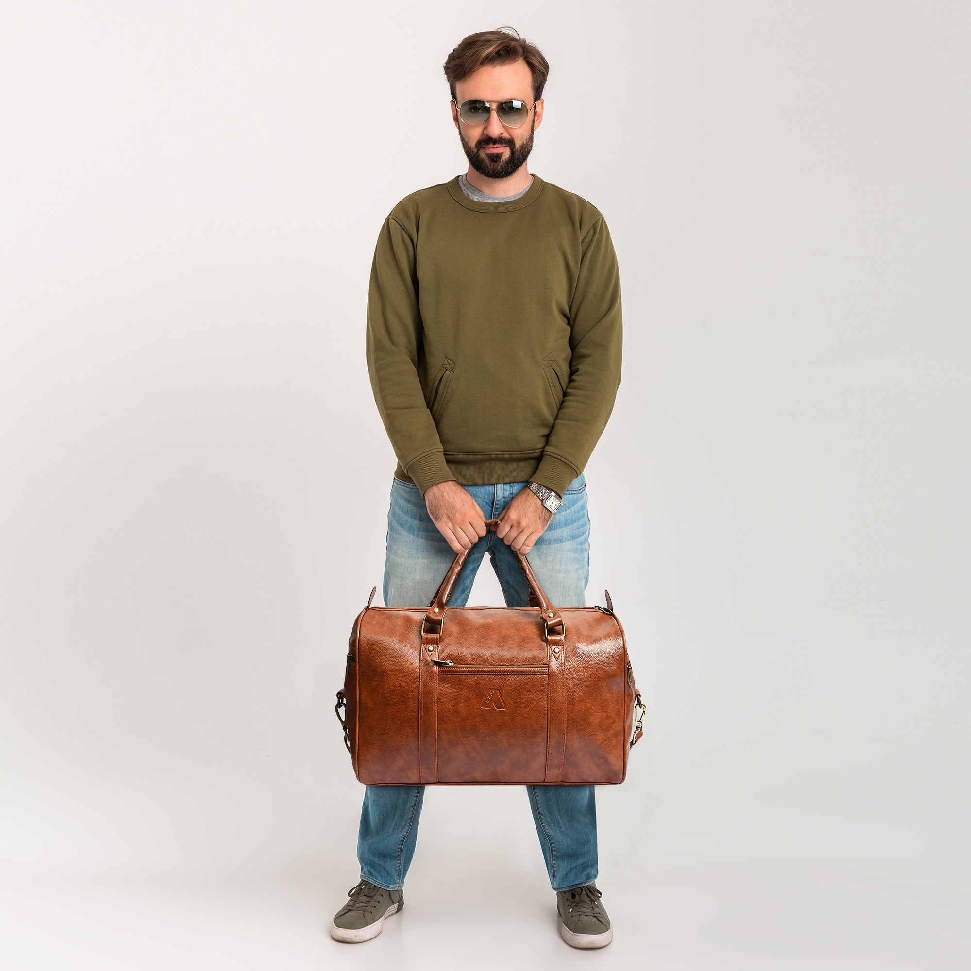 handsome confident bearded stylish man in sweatshirt with travel bag, wearing jeans and sunglasses isolated on white background