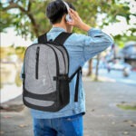Asian male traveler listening to music though his headphones while strolling around the city. back view
